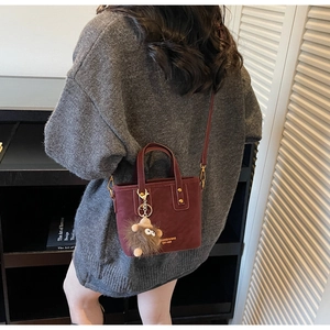 Detail of a burgundy bucket bag with plush monster charm and branded logo lettering