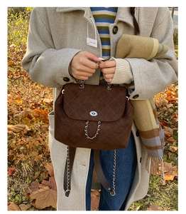 Detail of dark brown suede backpack with quilted stitching and gold chain strap in nature