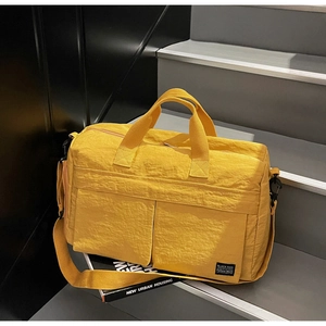 Detail of yellow nylon travel bag with front pockets and adjustable strap on a grey step