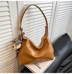 Detail of tan brown leather hobo bag with teddy bear charm on white book background