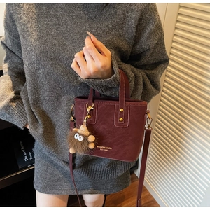 Detail of burgundy leather bucket bag with gold logo and brown plush monster charm