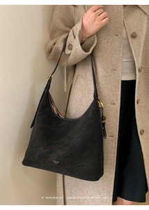Detail of black hobo bag showing contrast white stitching and gold brand logo on matte leather