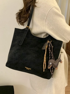 Black suede tote bag with adjustable strap and cute charms shown on model's shoulder
