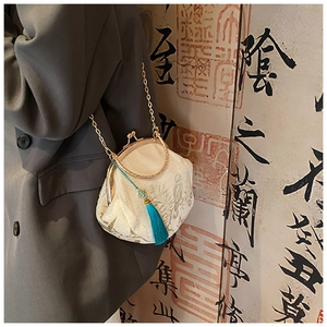 Detail of embroidered beige silk shell bag with golden floral patterns and blue tassel