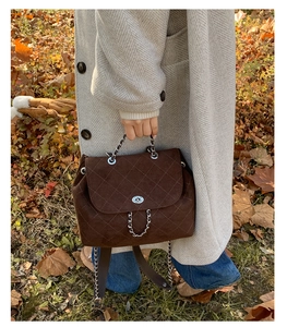 Detail of coffee quilted backpack with silver twist lock on autumn leaf background