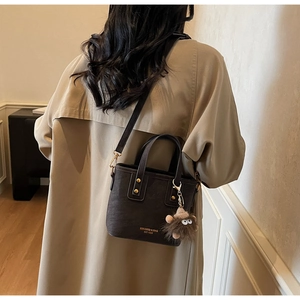 Detail of dark brown crossbody bag with gold text and a cute brown plush pendant