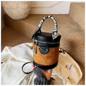 Macro detail of cylinder bucket bag featuring brown suede quilting and scarf handle