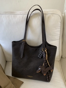 Retro dark brown pebbled leather tote bag with dachshund charm on a white sofa