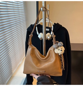 Detailed shot of brown leather shoulder bag featuring a dog plush and leopard bow charm