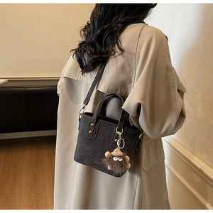 Detail view of brown pebbled leather crossbody bucket bag with plush monster charm