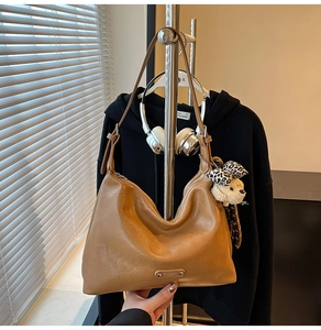 Detail of camel leather shoulder bag featuring a metallic logo and cute bear charm
