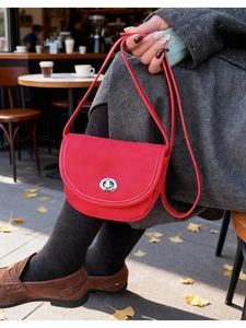 Detail of red saddle crossbody bag with silver rotating lock on grey coat background