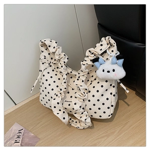 Close-up of white polka dot shoulder bag with pleated strap and plush doll charm