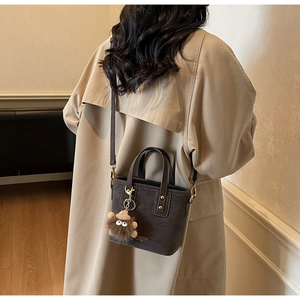 Detail of grey crossbody bucket bag with plush charm and brand text on trench coat