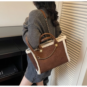 Detail of a brown faux suede tote bag with white faux fur trim and gold chain accent