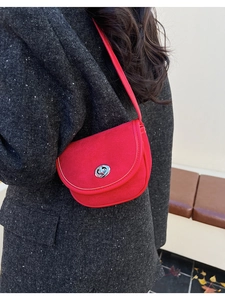 Close-up of red suede saddle bag with silver twist lock on a grey tweed blazer
