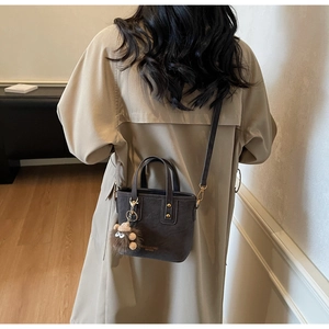 Retro grey matte tote bag with plush monster charm worn over a khaki trench coat