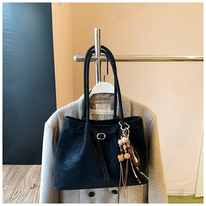 Detailaufnahme einer schwarzen Wildleder-Shopper-Tasche mit Blumenanhänger und Metallschnalle