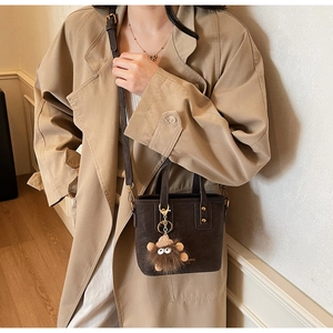 Detail of dark brown suede bucket bag with a cute monster plush charm on long strap