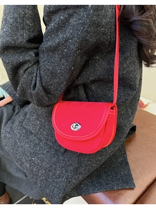 Detail of red suede crossbody saddle bag with silver clasp styled on a grey tweed coat