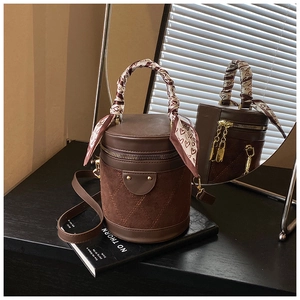 Detail of a brown cylindrical bucket bag with heart pattern scarf and gold hardware