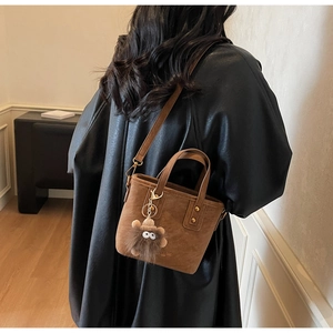 Detailed view of brown suede bucket bag with plush charm on a black leather jacket