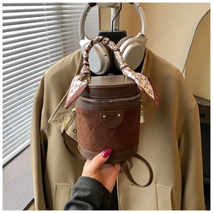 Detail of a brown quilted cylinder bucket bag with a heart-patterned silk scarf on the handle