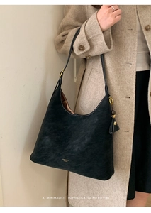Detail of a vintage black frosted shoulder bag with white stitching on a beige coat