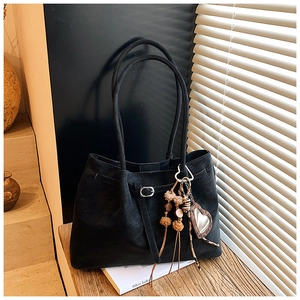 Detail der schwarzen Wildleder-Tote Bag mit Silberschnalle und Herzanhänger auf Holz