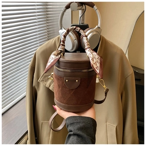Detail of a brown cylindrical bucket bag with quilted suede and silk scarf handle