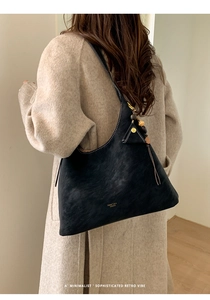 Close-up of matte black suede bucket bag with gold logo and beaded accessory detail