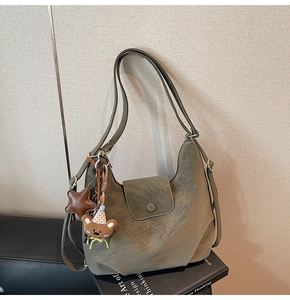 Détail d'un grand sac hobo vert vintage avec breloque ours posé sur des livres anglais