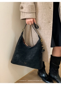 Detail of black suede hobo bag with white contrast stitching and gold logo lettering