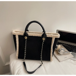 Detail of black suede tote with white faux fur trim and gold chain strap in workspace