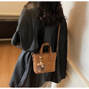 Brown suede bucket bag detail with golden rivets, plush charm, and thin shoulder strap