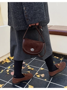 Detail of a brown suede saddle bag with a silver rotary lock shown in an outdoor setting
