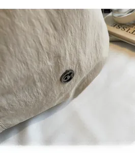 Detail of minimalist metallic 'M' logo and textured fabric on a beige tote bag