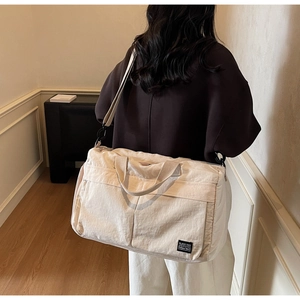 Detail view of large beige nylon travel bag showing shoulder strap and side brand label