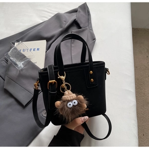 Detail of black crossbody bucket bag featuring gold logo and cute brown plush monster charm