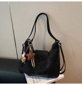 Détail d'un sac hobo en cuir noir avec breloques étoiles posé sur des livres