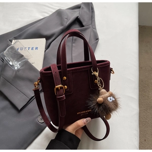 Detail of dark red bucket bag featuring gold logo and cute plush monster charm
