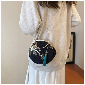 Close-up of black shell bag with embroidery, gold chain strap, and blue silk tassel