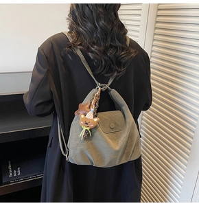 Sac à dos vert olive avec breloque ours porté sur un manteau d'hiver noir en laine