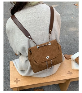 Detailed back view of brown suede quilted backpack with metal chain straps in a park