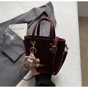 Detail of burgundy suede bucket bag with plush monster charm and golden hardware