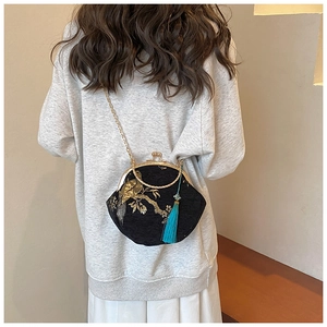 Detailed embroidery of birds and flowers on a black shell bag with turquoise tassel