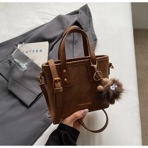 Detail of a brown bucket bag with a plush charm and adjustable strap in a fashion setting