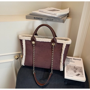 Detail of winter suede tote bag with faux fur trim and gold chain strap on white shelf