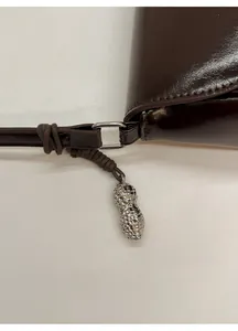 Macro detail of dark brown leather handbag with a silver peanut charm and metal hardware