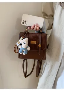 Detail of dark brown faux suede backpack featuring a gold nameplate and a teddy bear charm